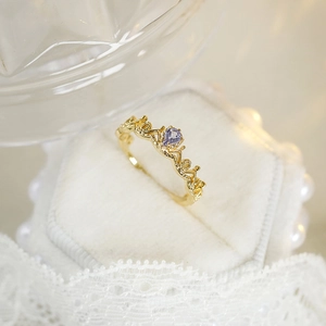Detail of a gold crown ring with a pear-shaped purple gemstone on white velvet