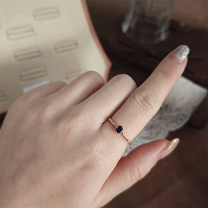Primo piano di anello dorato con pietra arenaria blu su un dito di modella e sfondo vintage