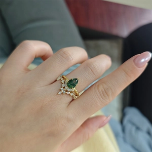 Close-up of a pear-cut moss agate ring set with gold twisted band on a hand
