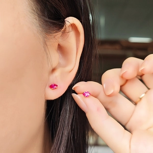 Macro view of oval red ruby earrings in gold four-prong setting for a minimalist style