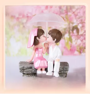 Miniature PVC wedding couple figurines sitting on a stone bench holding a pink umbrella