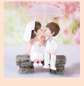 Detail of cute PVC wedding couple figurines sitting on stone bench under a pink umbrella