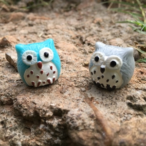 Close-up of blue and grey resin owl figurines in a natural rock miniature garden