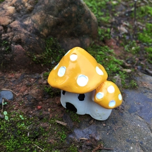 Macro detail of a yellow resin mushroom house ornament in a natural mossy garden setting