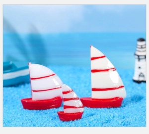 Detailansicht von drei roten Miniatur-Segelbooten aus Harz auf blauem Deko-Sand