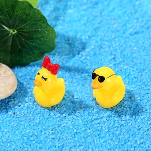 Figurines de canards en résine avec nœud et lunettes sur paysage de sable bleu