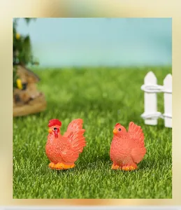 Miniature resin rooster and hen figures on green grass with farm fence background