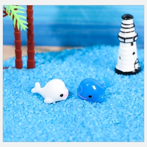 Miniaturas de ballenas de resina en paisaje de arena azul con faro y palmera