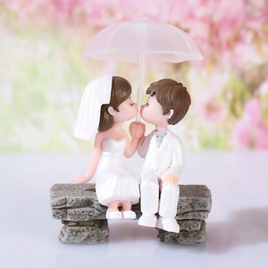 Miniature wedding couple figurine sitting on a bench with a pink umbrella decor