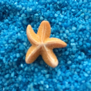 Deko-Seestern aus orangefarbenem Harz auf blauem Deko-Sand für mediterranes Flair