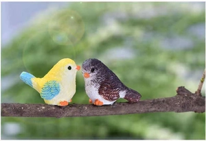Detail of two colorful resin bird figurines perched on a natural wooden branch