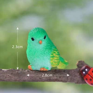 Detail view of a cute green resin bird miniature on a branch with size 2.3x2.8cm