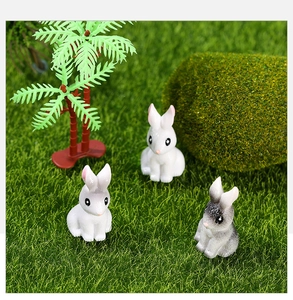 Macro detail of miniature resin rabbits on green moss with decorative palm tree