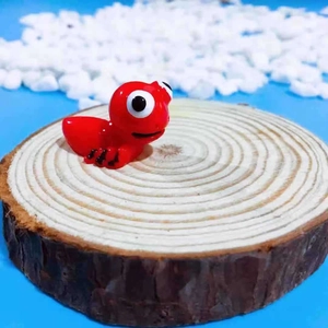 Close-up of a cute red resin ant figurine with big eyes on a wooden coaster display