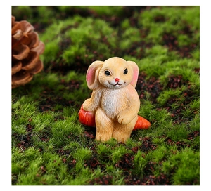 Close-up of a mini resin bunny figurine holding a carrot on green moss background