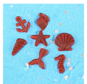 Macro detail of red translucent resin starfish and shell charms on blue sand