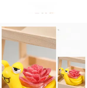 Detail of cute yellow snail figurine with pink artificial succulent on wooden shelf