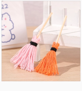Macro shot of miniature handmade broom with pink and orange cotton tassels and wooden handle