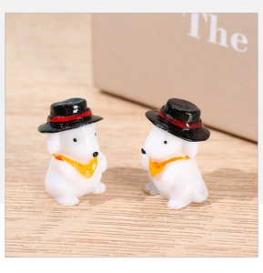 Close-up of two miniature resin puppy figurines wearing black hats on a wooden surface
