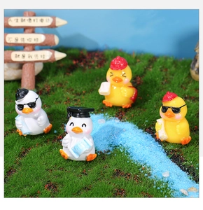 Miniature resin duck figurines featuring graduation caps and sunglasses in a micro landscape