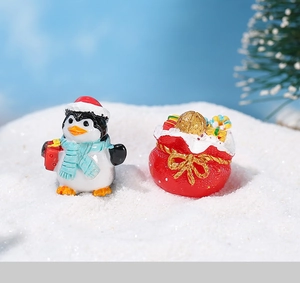 Close-up of resin Christmas penguin and red gift bag figurines in snow scene