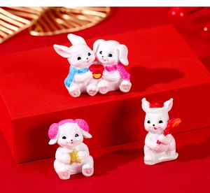 Three cute white resin bunny figurines with festive hats and scarfs on a red gift platform