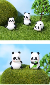Macro shot of miniature panda figurines with pink cheeks in a lush green moss micro landscape