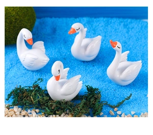 Close-up of four white resin swan figurines with orange beaks on blue sand