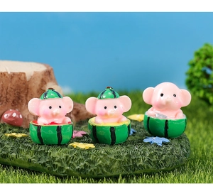Three cute miniature pig figurines in watermelon shells on artificial grass landscape