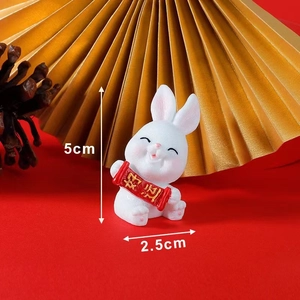 Close-up of a white resin rabbit figurine holding a Good Luck scroll on red background