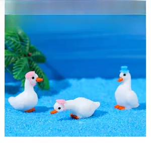 Micro landscape resin white swan figurines with colorful hats on a beach scene