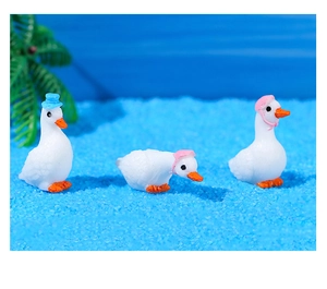 Miniature resin white duck figurines wearing hats on beach sand with palm trees