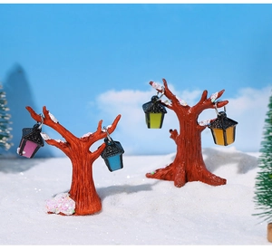Détail de sapins enneigés miniatures en résine avec lanternes colorées pour décor d'hiver