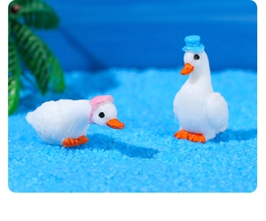 Detail of miniature resin swans wearing pink and blue hats on a blue sand landscape