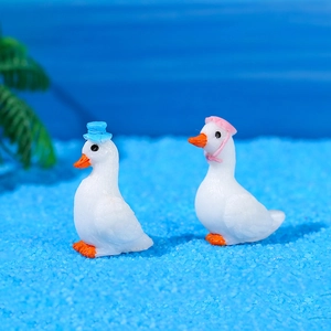 Miniature resin white swan figurines with hats on blue sand beach setting