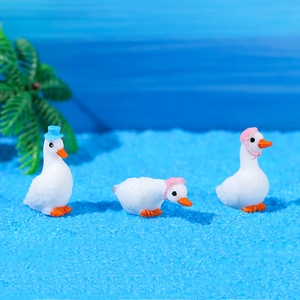 Three miniature white swan figurines with hats on blue sand micro landscape decoration
