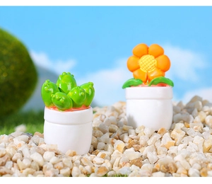 Macro detail of miniature dollhouse cactus and orange flower in white pots on pebbles