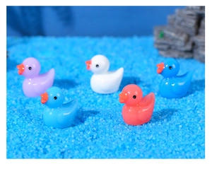 Group of colorful miniature resin ducks in purple blue and pink on sand background