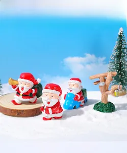 Dettaglio di tre statuine di Babbo Natale in resina con mini albero su base di legno