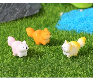 Vista dettagliata di tre figurine di volpe in resina colorata su erba verde artificiale