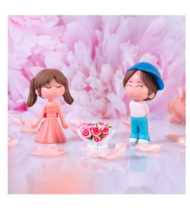 Close-up of couple figurines with girl in pink dress and boy in blue cap among roses