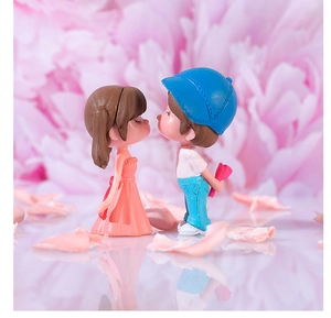 Close-up of cute couple figurines with a girl in pink dress and boy with rose on white surface