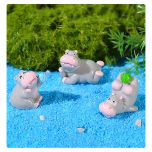 Trois figurines mini-hippopotames mignons sur du sable bleu et de la mousse verte