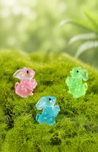 Macro shot of colorful luminous resin rabbits on moss for fairy garden decor