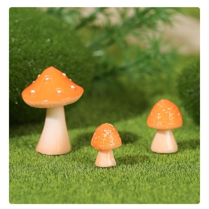 Three miniature resin mushroom ornaments with orange caps on artificial green grass