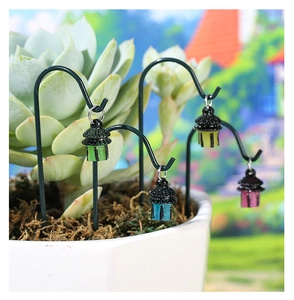 Detailed view of miniature luminous lanterns on metal hooks in mossy succulent pots