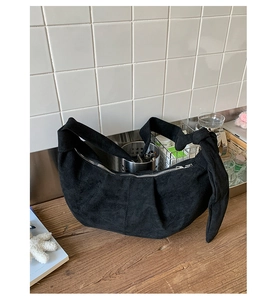 Detail of a black suede crescent hobo bag with a knotted strap and silver zipper closure