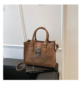 Détail du sac cabas en cuir avec crâne en métal et rivets posé sur un livre