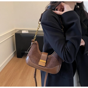 Detail of brown suede and leather crossbody bag with vintage gold buckle and chain