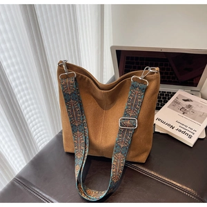 Brown canvas bucket bag with vintage patterned wide strap on a leather seat next to books